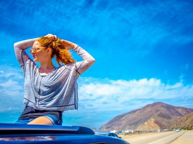 woman in grey and black plaid shirt sitting on car hood during daytime