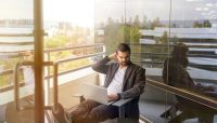 man sitting on gray arm chair using silver laptop computer on building balcony at daytime
